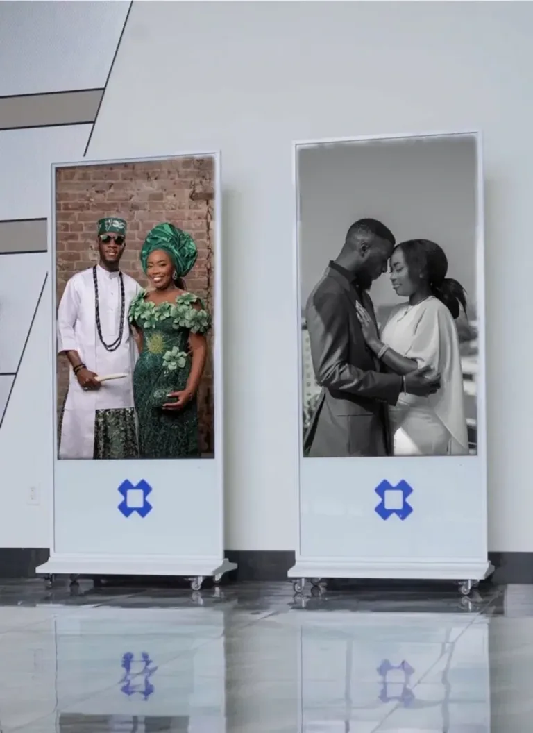 Two real BlueBox 65-inch white-framed digital display totems, with screens above solid bases, at an event venue